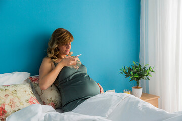 A pregnant woman in bed taking a photo of her belly with phone.