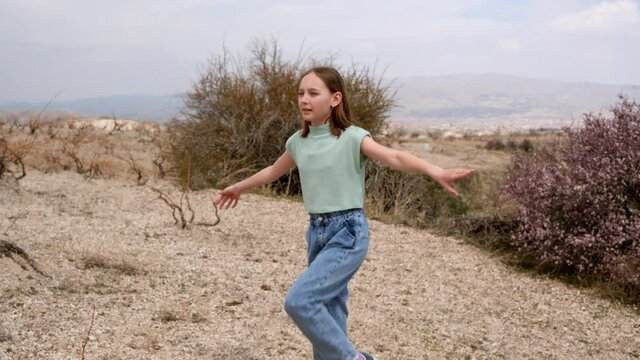 Girl performing leg exercise in natural landscape. Beautiful sporty teenage girl in t-shirt and denim pants training in deserted valley