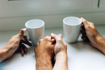 male couple holding hands with a cup of coffee or tea - gay relaxing at the home cafe or hotel