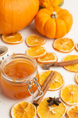 Aerial view of pumpkin jam jar on white table with orange slices, canala and pumpkins, white background, vertical