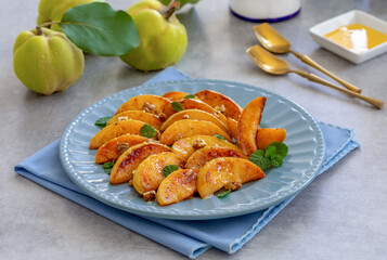 Quince Dessert. Sliced caramelized quince served with honey and nuts on a plate with fresh fruits on background. Selective focus, gray concrete table.