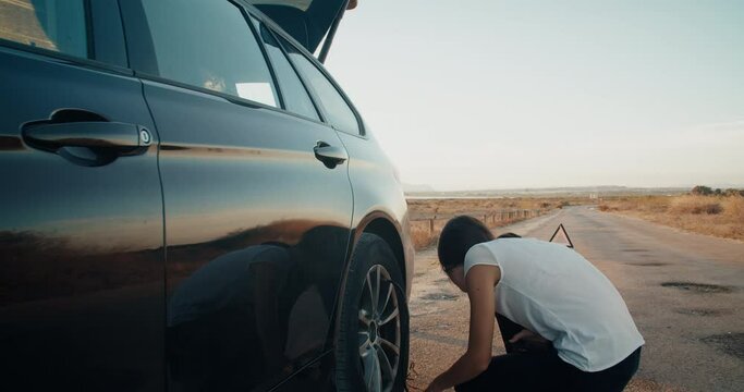 Young attractive woman during travel has vehicle breakdown flat tire inflates the wheel using automatic compressor. Concept of broken car on road an fix it by your self