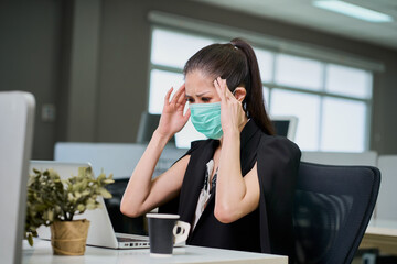 Businesswoman wear facial mask has headache action while working with laptop in business office