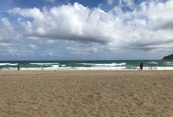 Fototapeta na wymiar Big white clouds over a sandy beach in a windy day. Agitated sea with foam waves at sandy beach.