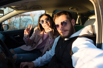 Happy young couple taking selfie in car at sunset in countryside. Travel, road trip and comfortable concept