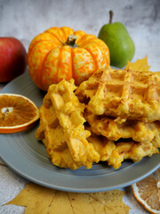 Belgian gluten-free pumpkin waffles lie on a gray plate with a dry slice of lemon, pear, apple and anise stars on a gray table. maple leaves
