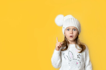 Portrait child girl with finger pointed up in winter knitted hat with pompon pose has idea isolated light yellow background. Christmas New Year shopping sale,promotion