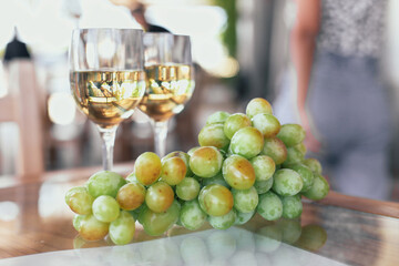 Two glasses of white wine, green grapes on a wooden table on a vineyard