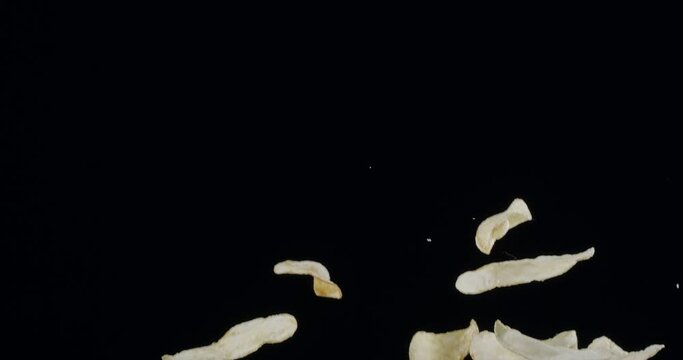 Natural potato chips rise and fall against a black background. Slow Motion 300 fps Blackmagic Ursa Pro G2.