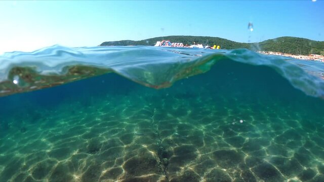 Slow-motion half underwater video at the border of air and water. Beautiful rocky beach on the Adriatic Sea in Montenegro.