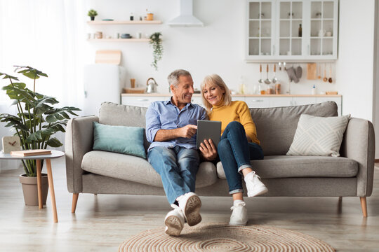 Cheerful Mature Spouses Using Digital Tablet At Home