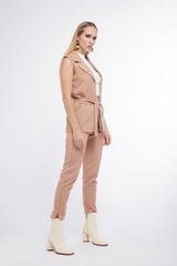High fashion photo of a beautiful elegant young woman in a pretty beige suit, pants, trousers, vest, boots posing over white, soft gray background. Studio Shot, portrait. Blonde