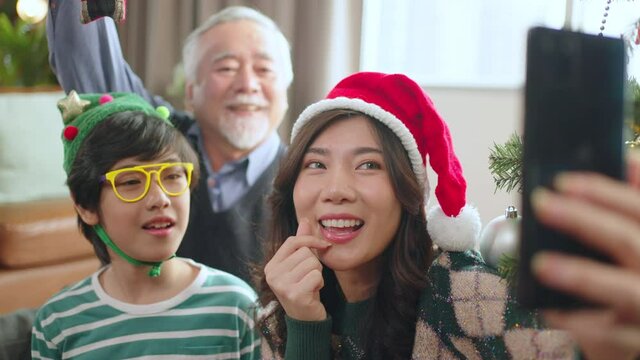 Asian multi generation family parent and grand parent sit relax smile together fun and using smartphone talking selfie photo happiness together livingroom at home during christmas thanksgiving weekend
