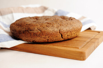 Fresh homemade round malted rye bread on wooden board. White background, linen fabric