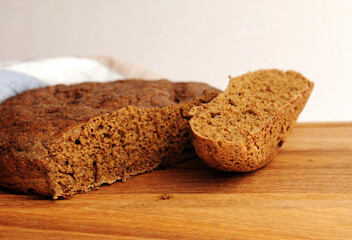 Fresh homemade round malted rye bread on wooden board. White background, linen fabric