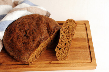 Fresh homemade round malted rye bread on wooden board. White background, linen fabric
