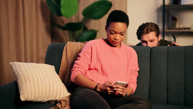 Jealous boyfriend trying to read messages on the mobile phone of his girlfriend while she is not watching. Interracial couple. High quality 4k footage