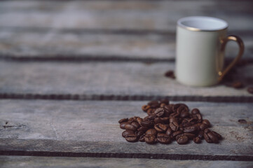 Hot coffee in mini white coffee cup and coffee beans in a heart shape on a rustic wooden background with copy space