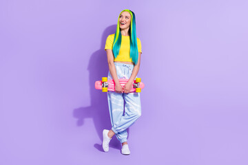 Full length body size view of attractive cheerful girl holding skateboard fantasizing isolated over violet purple color background