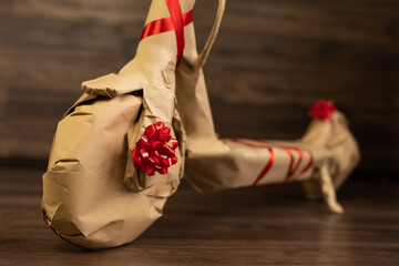 Rustic recycled Christmas new year gift, ecological scooter wrapped in brown paper and tied with red ribbon with bow. Transport of future. Holiday present. Care package. Vintage parcel.