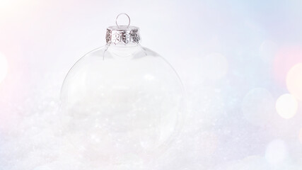 Transparent glass Christmas ball on the snow on a light background. Close-up.Christmas and New Year Shiny, Glitter ,bokeh effect background.Greeting card, banner, poster.Soft focus.copy space.concept