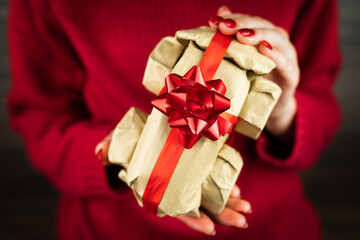 Young woman in red sweeter holding a toy car wrapped in eco rustic beige recycled brown paper and tied with a red ribbon with a bow. Christmas, New Year, Birthday, Valentine's Day concept. Close-up