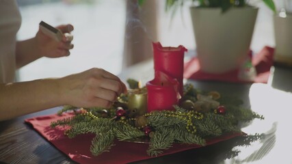 An unrecognizable girl blows out an evergreen wreath with two red candles and one golden candle. Christmas traditions and customs of Christians on the eve of the holiday. A symbol of the holiday.