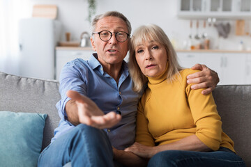 Discontented Senior Couple Talking To Camera Sitting At Home - obrazy, fototapety, plakaty