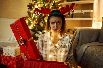 Portrait of displeased upset female frowns face as disappointed, hold dislike gift on Christmas