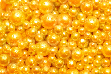 Beautiful background with pearl gold pearls, top view. Abstract texture for festive backgrounds. Shiny yellow surface of Christmas decorations. Gems close-up. Golden bright background.