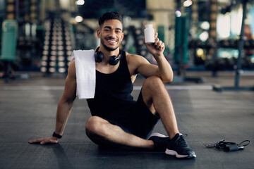 Fototapeta na wymiar Young Muscular Arab Man Holding Container With Supplement Pills, Posing At Gym