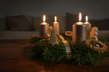 Golden candles on an advent wreath with some natural Christmas decoration on a wooden coffee table...