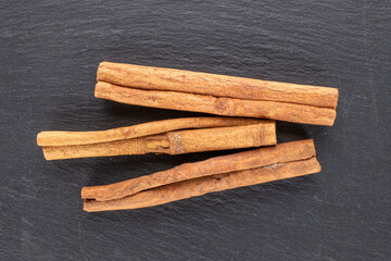 Three sticks of fragrant cinnamon on a slate stone, close-up, top view.