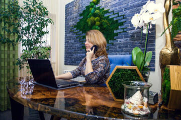 A young woman interior designer is working and talking on the phone in her office at a computer.