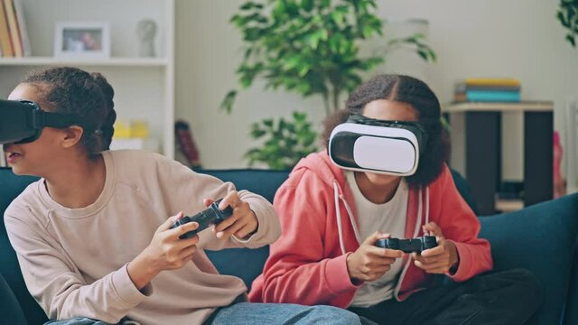 Two excited teenage girls playing video game together, wearing vr headsets