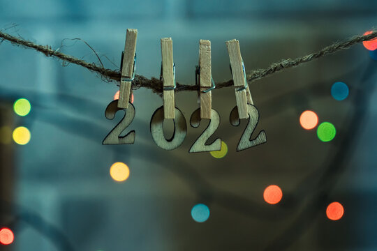 On a string of wooden clothespins hung wooden numbers 2022. In the background are multicolored lights of the garland. Happy New Year.