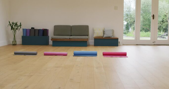 Four rolled up yoga mats in empty studio with wooden floor and doors to garden