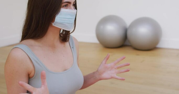 Caucasian female yoga instructor in face mask talking during yoga class