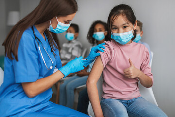 Korean Preteen Girl Getting Vaccinated Gesturing Thumbs-Up In Clinic Indoors