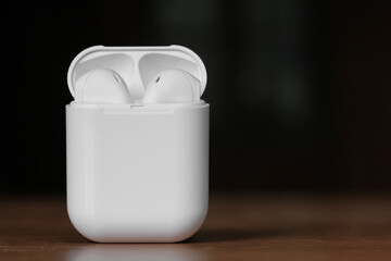 White color true wireless earphone in opened charging case ready for pairing on wooden table. Copy...