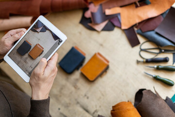 Top view male tanner use tablet at leather workshop. Craftsman creating online advertising promotion