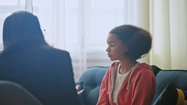 Female therapist talking to upset teen girl at counselling session, psychology