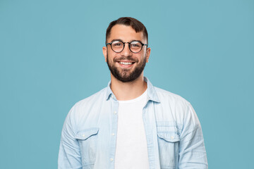 Smiling friendly mature caucasian male in glasses looking at camera, isolated on blue background
