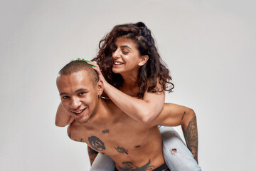Young couple, tattooed guy and his girlfriend with curly dark hair having fun while posing together isolated over gray background