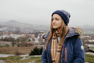 Beautiful young woman in blue coat, scarf and hat. Wet hair at rainy day in Norway. City in background.