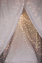 Beautiful indoor interior christmas decorations in bedroom. Boho bed with canopy decorated with string lights ready for celebration