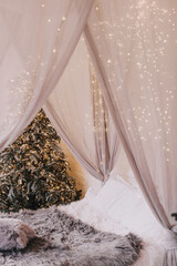 Beautiful indoor interior christmas decorations in bedroom. Boho bed with canopy decorated with string lights ready for celebration