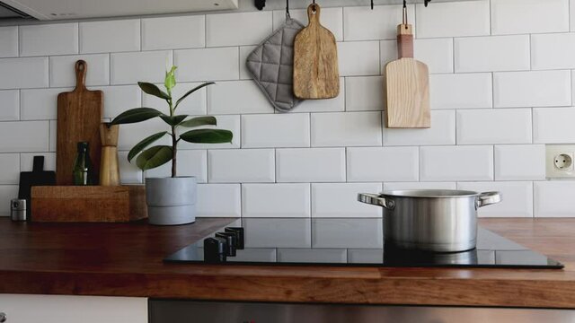 Kitchen brass utensils, chef accessories.Water boils in a saucepan. Hanging kitchen with white tiles wall and wood tabletop.Green plant on kitchen background
