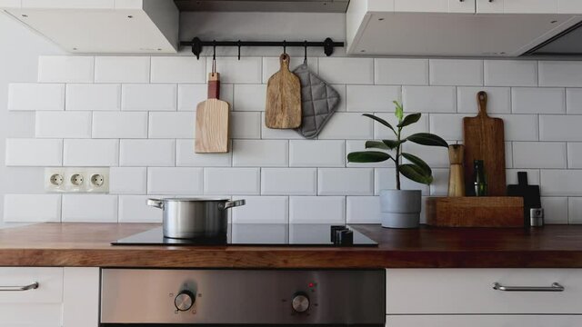 Kitchen brass utensils, chef accessories.Water boils in a saucepan. Hanging kitchen with white tiles wall and wood tabletop.Green plant on kitchen background