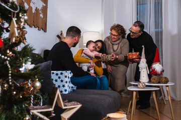 Parents, daughter and grandparents at Christmas giving a gift to the baby with a Christmas tree in front